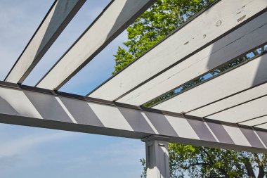 Geometrik tasarımı olan güneş ışığı beyaz pergola, 2015 yılında Indiana 'nın verimli bir bahçe bölgesinde mavi bir gökyüzü zeminine keskin gölgeler serpiştiriyor..