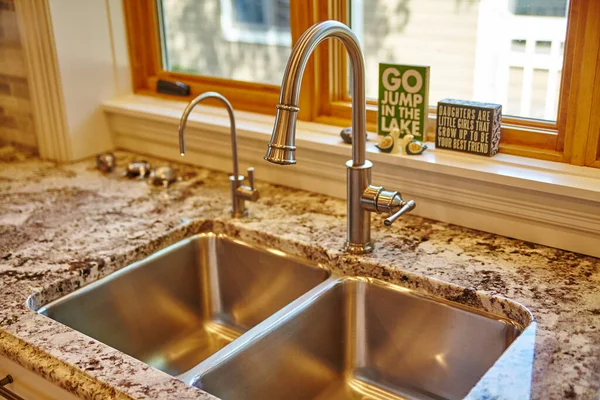 Modern kitchen sink area with a stainless steel basin, high-arc faucet on a polished granite countertop, and decor with warm family messages, in a residential home s, Indiana, 2015.