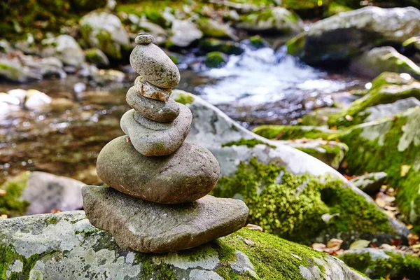 Balanced stone cairn on mossy rock with serene stream backdrop, captured during a tranquil hike on the Smoky Mountains Little River Trail, Tennessee, 2015.