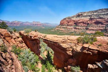 Sedona, Arizona 'daki doğal kırmızı kumtaşı kemeri Devils Köprüsü' nün gün ortasında nefes kesici manzarası, manzaralı bir çöl manzarasıyla çevrili..