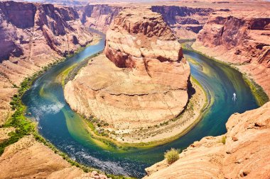 2016 'da Colorado Nehri' ndeki görkemli Horseshoe Virajı 'nın güneşli manzarasında Arizona' nın yüksek kızıl kayalıkları arasında küçük bir tekne vardı.