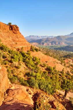 Sedona, Arizona 2016 'daki görkemli Katedral Kayası' nın güneşli gündüz manzarası açık mavi gökyüzüne karşı seyrek yeşil kayalıklarla çarpan kırmızı kumtaşı uçurumunu gözler önüne seriyor.