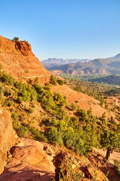 Sedona, Arizona 2016 'daki görkemli Katedral Kayası' nın güneşli gündüz manzarası açık mavi gökyüzüne karşı seyrek yeşil kayalıklarla çarpan kırmızı kumtaşı uçurumunu gözler önüne seriyor.