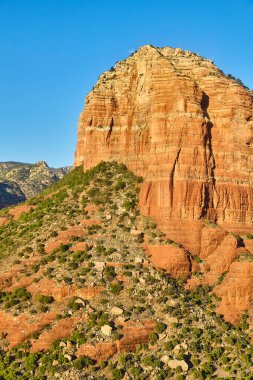 Sedonas Bell Kayası, parlak mavi gökyüzünün altında çarpıcı bir çöl simgesi katmanlı kırmızı kayaları ve seyrek yeşil bitki örtüsünü sergiliyor, 2016