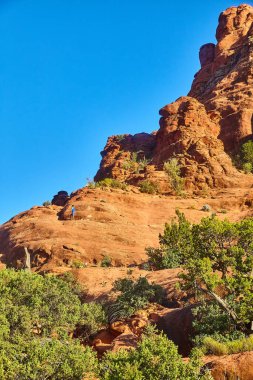2016 yılında Sedona, Arizona 'da Bell Rock' ı keşfeden yalnız yürüyüşçü, açık mavi gökyüzü altında engin çöl manzarasını ve engebeli kızıl kaya oluşumunu sergiliyor.