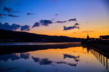 Sabahın erken saatlerinde Houghton, Michigan 'da sakin bir su üzerinde gün doğumu, sakin bir gökyüzünü ve ahşap iskele siluetini yansıtıyor..