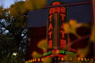 Ann Arbor, Michigan şehir merkezinde şehir yeşillikleriyle çerçevelenmiş gece gökyüzünde parlayan neon ışıklı Devlet Tiyatrosu tabelası