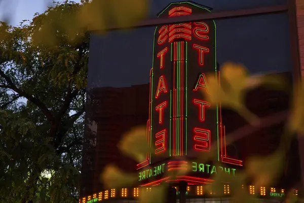 Ann Arbor, Michigan şehir merkezinde şehir yeşillikleriyle çerçevelenmiş gece gökyüzünde parlayan neon ışıklı Devlet Tiyatrosu tabelası