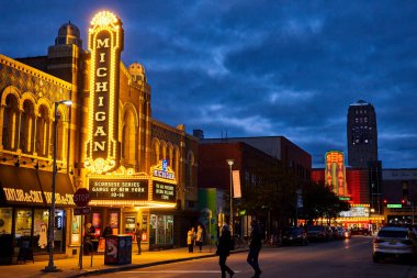 Ann Arbor 'un üzerine alacakaranlık düşüyor, Michigan Tiyatrosu ve eyalet tiyatrosu neon tabelaları tarihi şehir merkezindeki hayat dolu sokak manzarasını aydınlatıyor..