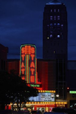 Gün batımı Ann Arbors 'un tarihi Devlet Tiyatrosu' na iniyor. Neon tabelası şehir merkezini aydınlatıyor. Arka planda ikonik Burton Anıt Kulesi var..