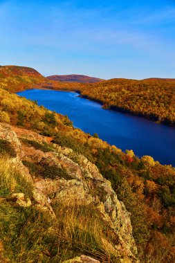 Clouds, Michigan 'daki Gölü' nün canlı sonbahar manzarası - Berrak mavi bir gökyüzünün altında, renkli ve yoğun bir ormanın ortasındaki dolambaçlı bir nehrin sakin manzarası.