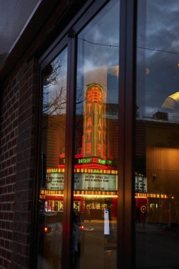 Ann Arbor şehir merkezindeki neon ışıklı devlet tiyatrosu afişinin canlı yansıması alacakaranlıktaki hareketli şehir yaşamını yakalıyor..