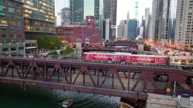 Gün batımında canlı bir Chicago manzarası, ikonik kanalı vurguluyor, Wells Caddesi Köprüsü 'nde hareketli bir tren ve aydınlatıcı şehir ışıkları..