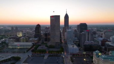Indianapolis, Indiana 'da alacakaranlık renkleri sergilenen hava yayası çekimi. Önemli noktalar arasında Indiana Eyalet Binası, parlayan şehir silueti ve günden geceye huzurlu geçiş yer alıyor..