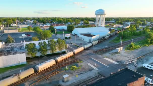 インディアナ州ミュンシーの産業を通過する賑やかな列車を明らかにするエアリアルフライオーバー 黄金の時間の光の中で象徴的なアメリカの水塔 — ストック動画