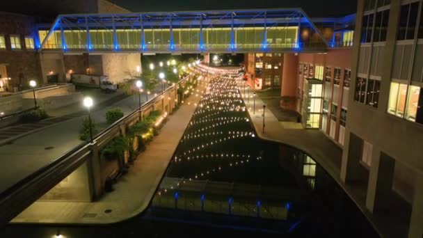 インディアナポリスの空中ペデスタルショットは夜にダウンタウンの運河エリアを魅了し 現代的なブルーリットの歩行者橋 活気に満ちた都市の建物 静かな水路の反射を特徴としています — ストック動画