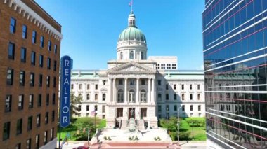 Indianapolis 'teki Indiana Eyalet Binası' nın havadan görünüşü, açık mavi bir gökyüzünün altında parlak bir şekilde ışıklandırılmış, neoklasik mimarisini şehir manzarasının ortasında sergiliyor..