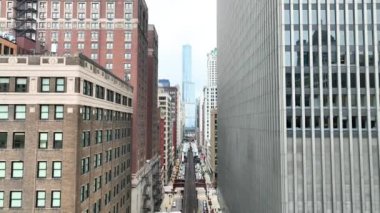 Chicago, Illinois şehir merkezinin havadan çekilmiş görüntüleri, şehrin tarihi ve modern mimarisini, ikonik tren raylarını ve hareketli caddeleri, bulutlu bir gökyüzü altında gözler önüne seriyor..