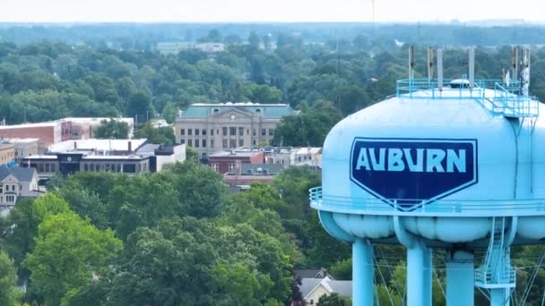 インディアナ州オーバーンに向かって飛ぶ空中飛行 象徴的な青い水タワーに向かって魅力的な小さな町の風景をグライドし 活気に満ちた日光を浴び 中西部の精神を捉える — ストック動画