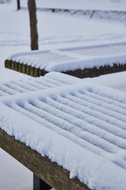 Freshly fallen snow blankets a serene wooden bench in downtown Fort Waynes Freimann Square, capturing a tranquil winter morning. clipart