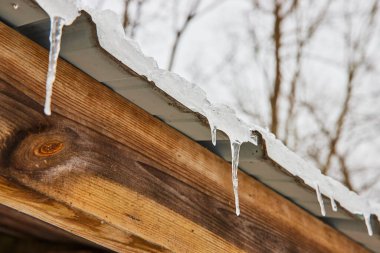 Winters Icy Touch on Rural Indiana - Detailed icicles dangle from a wooden roof, set against a backdrop of leafless trees at Cooks Landing County Park. clipart