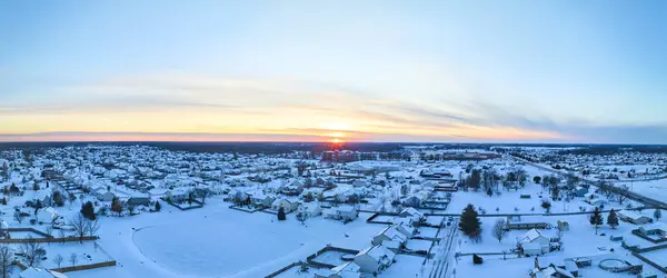 Aerial panorama of a snow-filled suburban neighborhood in Fort Wayne, Indiana, bathed in the warm glow of a winter sunset.