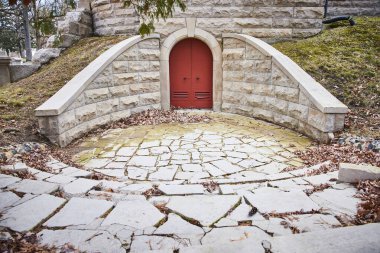 Enchanting red door in stone structure at Lindenwood Cemetery, Indiana, exuding a sense of mystery and tranquility amidst autumnal setting. clipart