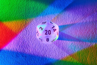 Vibrant 20-sided dice casting a rainbow spectrum on textured surface, symbolizing diversity, chance, and strategy in Fort Wayne, Indiana. clipart