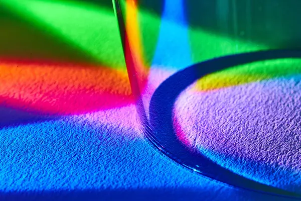 Abstract macro shot of light refracting through a wine glass creating a vibrant rainbow spectrum on textured surface, demonstrating color theory