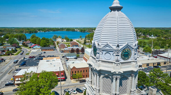 Aerial view of Warsaw, Indiana featuring the ornate Kosciusko County Courthouse, surrounded by a serene lake and vibrant town life.