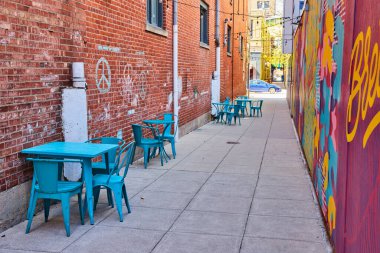 Vibrant alley in downtown Fort Wayne with colorful mural and turquoise cafe seating, showcasing urban renewal. clipart