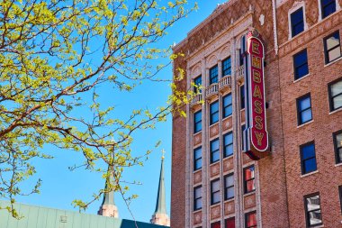 Fort Wayne şehir merkezinde bahar: Canlı mavi gökyüzü altında taze yeşilliklerle tarihi elçilik tiyatrosu.