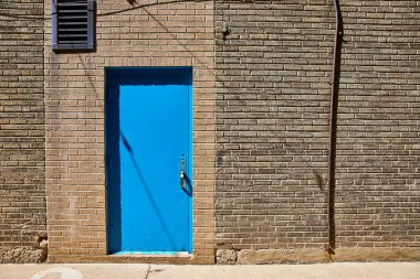 Fort Wayne, Indiana 'da, güneşli gökyüzünün altında dokulu tuğla bir duvarda parlak mavi bir kapı..
