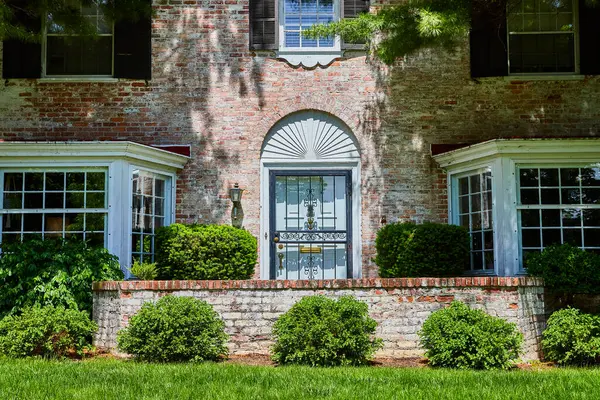 stock image Traditional brick house with ornate ironwork door in Fort Wayne, Indiana, showcasing suburban elegance and lush landscaping.