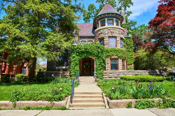 stock image Historic stone house with ivy in Fort Wayne, nestled in a lush garden under clear skies.