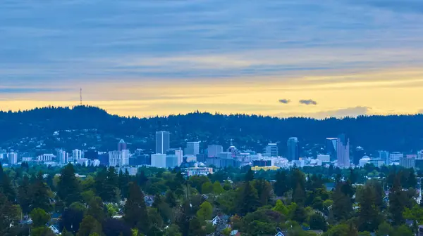 stock image Aerial view of downtown Portland, Oregon at golden hour, showcasing a stunning blend of modern high-rises and lush greenery against a backdrop of rolling hills and dense forest under a serene sky.