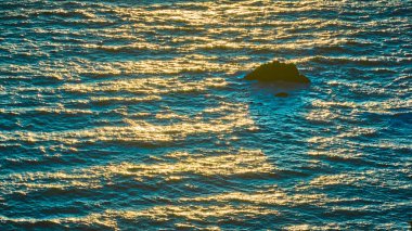 Güneş batarken Brookings, Oregon 'daki Arch Rock' ın hava görüntüsü. Güneş ışığı dalgalanan dalgalardan yansıyarak okyanusa altın renkler saçar. İzole kaya oluşumu biraz dinginlik ve esneklik ekler.