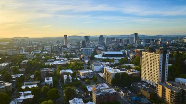 Stunning aerial view of downtown Portland, Oregon at sunrise, showcasing modern architecture, tree-lined streets, and a picturesque backdrop of rolling hills and distant mountains. Perfect for urban clipart