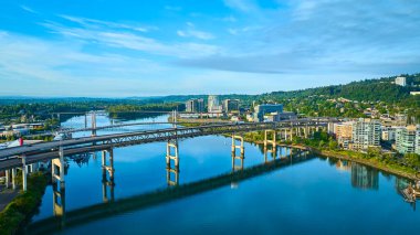 Portland, Oregon 'un çarpıcı hava manzarası Marquam Köprüsü' nü ve huzurlu nehir yansımalarını gösteriyor. Yüksek binaları ve yemyeşil tepeleri olan modern şehir manzarası şehir planlaması için mükemmel.