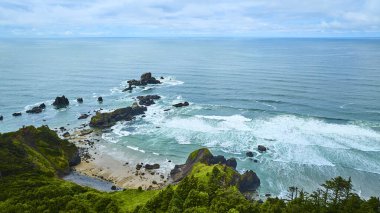Oregon 'daki Indian Beach' in hava manzarası. Bereketli yeşil uçurumlar ve dalgalı okyanus dalgalarının dağınık kaya oluşumlarına çarptığı engebeli kıyı şeridi. Seyahat ve çevre temaları için mükemmel.