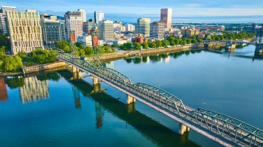 Portland, Oregon şehir merkezinin hava görüntüsü, sakin Willamette Nehri üzerindeki ikonik Hawthorne Köprüsü 'nü gösteriyor. Canlı ufuk çizgisi ve gür yeşillik şehirleri ve doğal uyumu vurguluyor..