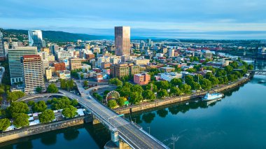 Aerial view of Portland, Oregon, showcasing the vibrant downtown with a mix of modern and classic skyscrapers. The Willamette River with a bridge and paddlewheel riverboat adds scenic beauty and clipart