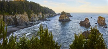 Altın saat sükuneti Arch Rock, Brookings, Oregon 'da. Engebeli kayalıklar, heybetli kaya oluşumlarıyla sakin denize iniyor. Çiçekli kozalaklı ağaçlar Samuel H 'deki bu güzel manzarayı çerçeveliyor.