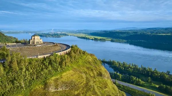 Crown Point, Oregon 'daki Vista House' un havadan görünüşü, Columbia River Gorge 'a bakıyor. Tarihi taş bina görkemli bir şekilde yeşil bir tepenin üzerinde duruyor, manzaranın büyüleyici manzaralarını sunuyor.