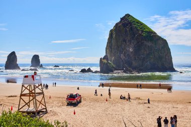 Oregon, Cannon Sahili 'nde coşkulu bir gün. Sahile gidenlerin üzerinde heybetli bir saman yığını var. Cankurtaran kulesi ve kurtarma aracı eğlence ve doğal güzellik sahnesinde güvenliği sağlar..