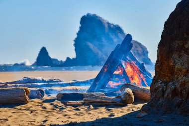 Serene beach bonfire at Harris Beach State Park, Oregon. Vibrant flames and bluish smoke under a clear sky create a mystical vibe, perfect for outdoor adventure and beach getaway themes. clipart