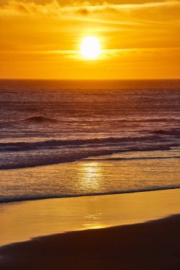 Gold Beach, Oregon 'da altın rengi günbatımı, yumuşak okyanus dalgalarından yansıyan kehribar renkleri. Yüksek bir bakış açısından sakin bir manzara batıdaki Meyers Creek Sahili 'nin huzurlu güzelliğini yakalıyor.