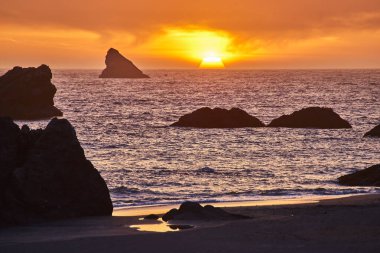 Günbatımı gökyüzünü Brookings, Oregon 'daki Harris Beach State Park' ın üzerine sıcak renklerle boyar. Engebeli kaya oluşumları okyanustan yükselir ve doğa, huzur ve huzur temaları için mükemmel sakin bir sahne yaratır.