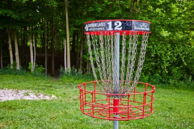 Huntington, Indiana 'daki Lush Memorial Park' ta 12 numaralı disk golf sepeti. Dinamik Diskler logolarına sahip canlı kırmızı çerçeve dingin bir orman zeminine karşı. Spor meraklıları ve doğa için mükemmel.