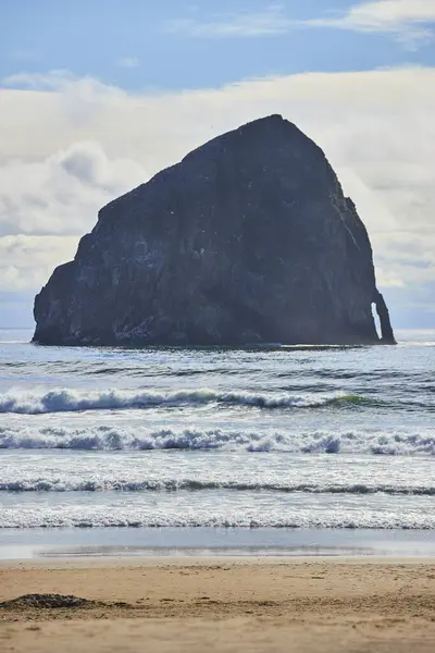 stock image A stunning coastal scene at Cape Kiwanda Drive in Pacific City, Oregon. Featuring a prominent sea stack, dynamic Pacific Ocean waves, and a serene sandy beach under a partly cloudy sky. Perfect for